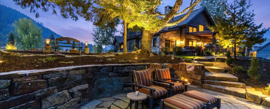 Beautiful cabin style golf course home with luxury finishes. Nighttime view with extraordinary landscaping lit up under a colorful sunset.